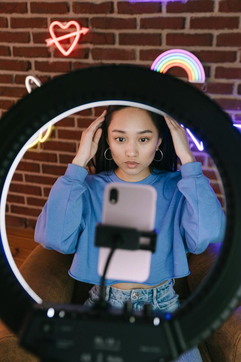 Asian woman recording a video with a smartphone and ring light for streaming purposes.